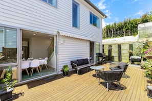 A modern house with a patio area featuring a dining table, chairs, a sofa, and a grill.