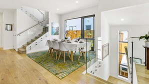 Un intérieur moderne avec un escalier, un coin repas et de grandes fenêtres.