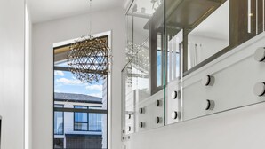 Un intérieur moderne avec un escalier, une porte à cadre noir, une petite table avec une plante et un luminaire suspendu.