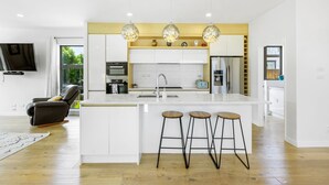 Une cuisine moderne dotée d’un îlot central, de tabourets de bar, de luminaires suspendus et d’un téléviseur à écran plat.