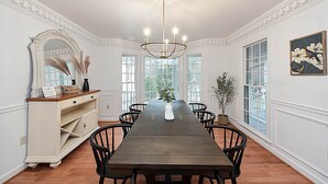 Un comedor con una larga mesa, sillas, un candelabro, un espejo y ventanas.