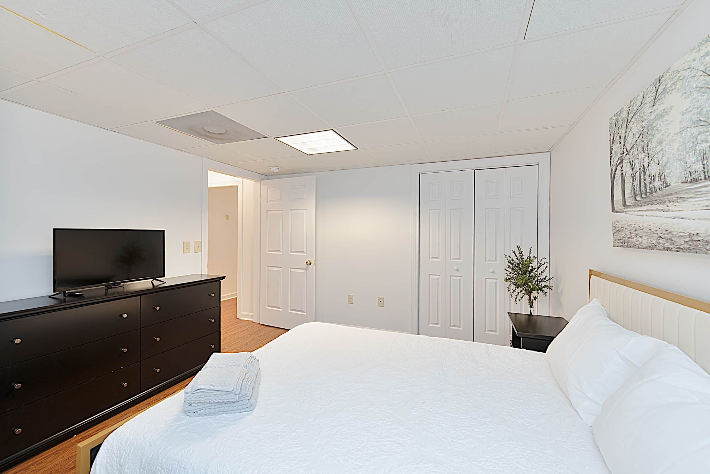 A bedroom with a bed, a dresser, a television, and a door leading to another room.