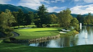 Un parcours de golf avec un étang, des arbres et des montagnes en arrière-plan.