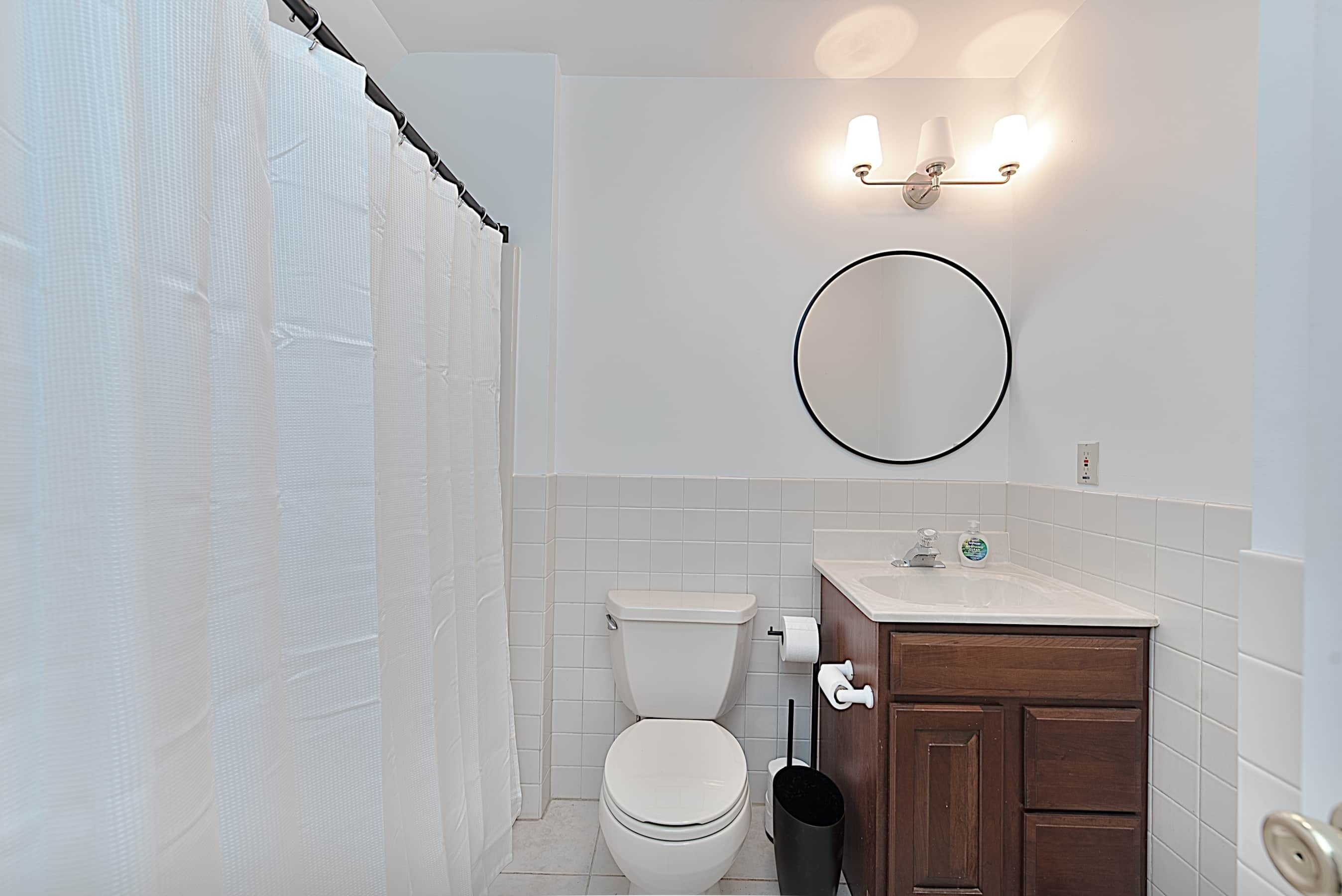 Un baño con inodoro, lavabo con espejo y cortina de ducha.