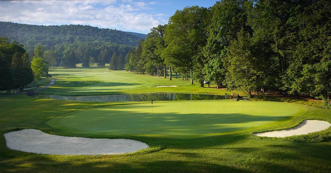 A golf course with sand bunkers, a pond, and dense trees in the background.