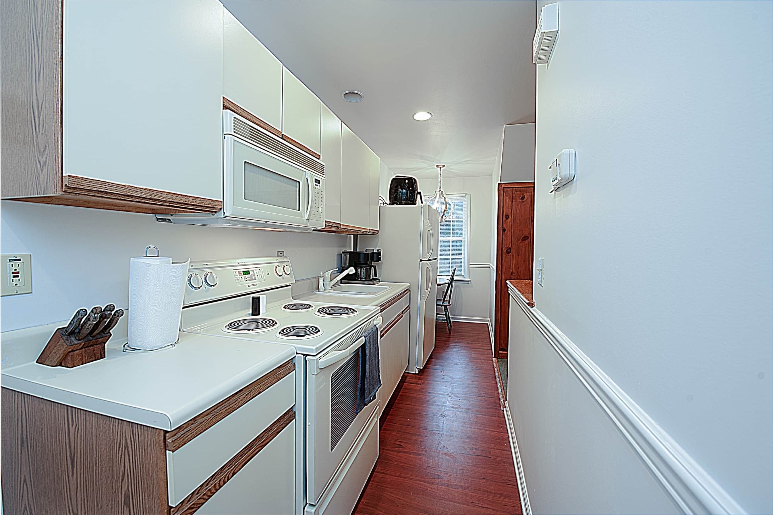 A narrow kitchen with white appliances, wooden cabinets, and a wooden floor.
