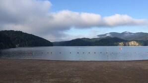 Un lago con orilla arenosa y boyas rojas en el agua.