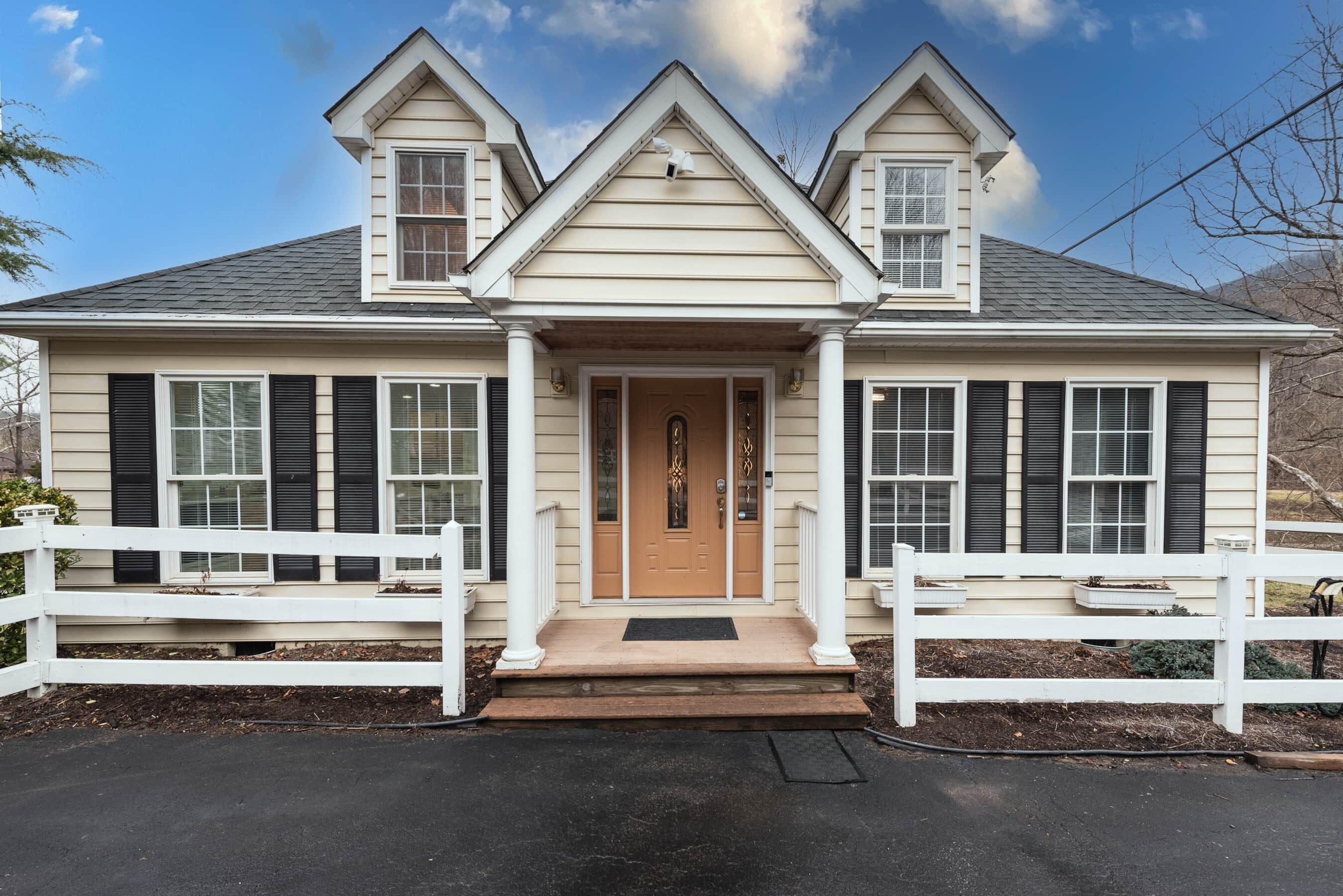 Une maison à deux étages avec une entrée centrale, une clôture en bois peinte en blanc et un jardin devant.