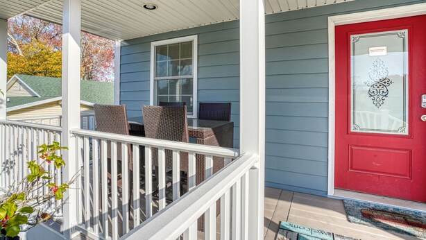 A porch with wicker furniture, a red door, and a white railing. - Beach Haven | Walk to Downtown Chincoteague, Wraparound Deck, Smart TVs & Garage for Beach Gear (Chincoteague Island)