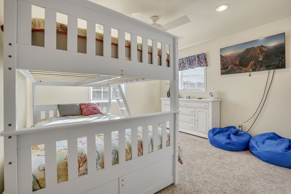A bunk bed with a ladder, a desk, a chair, and a blue bean bag chair in a room with a ceiling fan and a painting on the wall. - Beach Haven | Walk to Downtown Chincoteague, Wraparound Deck, Smart TVs & Garage for Beach Gear (Chincoteague Island)