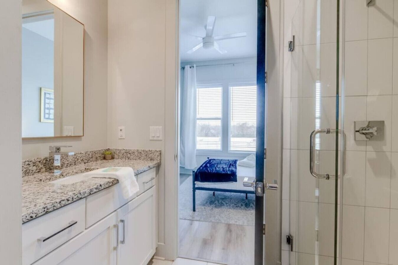 A bathroom with a granite countertop, a mirror, and a shower area with a glass door.