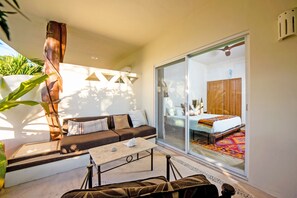 Un dormitorio moderno con un amplio ventanal corredera que da a un balcón, un sofá, una mesa de centro y una cama con un edredón de colores.