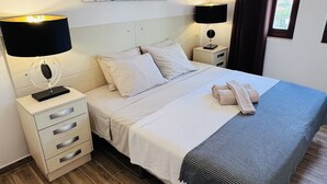 A neatly arranged bedroom with a bed, bedside tables, a nightstand, a wall-mounted artwork, and a window with curtains. - Charming 2 bedroom triplex in the Old Village, Vilamoura, Algarve (Vilamoura)