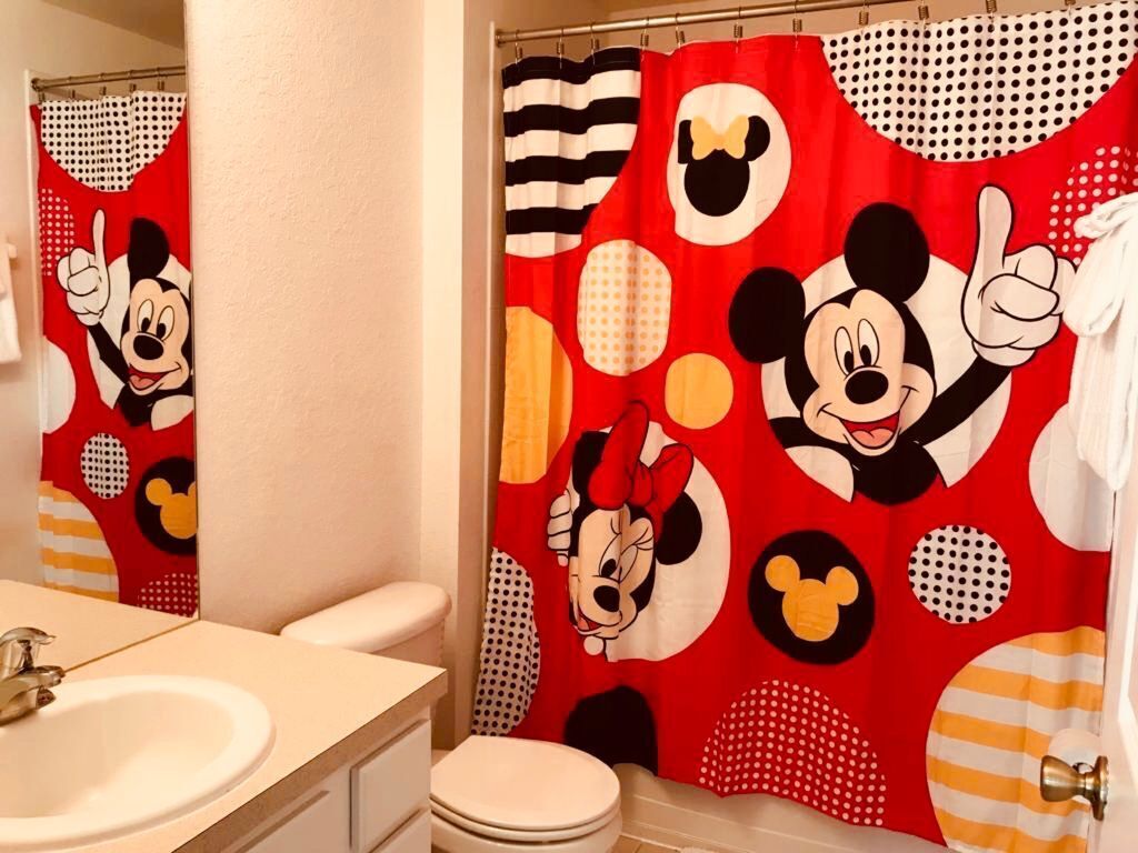 Une salle de bain avec un rideau de douche à l’effigie de Mickey Mouse, un lavabo blanc et des toilettes.