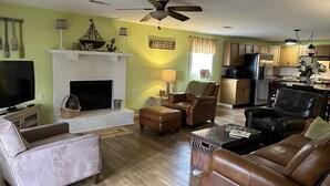 A living room with a fireplace, leather sofas, a television, and a kitchen in the background.