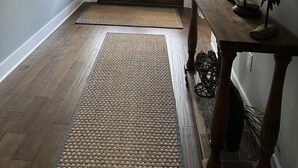 A hallway with a wooden floor, a woven rug, a wooden bench, a mirror, and a door with windows.