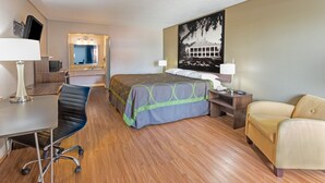 A hotel room with a bed, a desk, a chair, a sofa, a desk lamp, a nightstand, and a wall-mounted TV. - Super Place Inn (Opelousas)