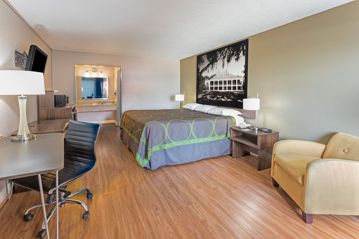 A hotel room with a bed, a desk, a chair, a sofa, a desk lamp, a nightstand, and a wall-mounted TV.