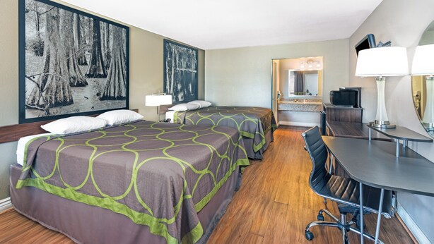 A hotel room with two beds, a desk, a chair, a TV, and a large framed picture on the wall. - Super Place Inn (Opelousas)