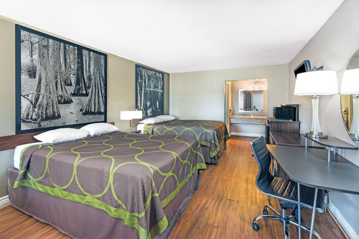 A hotel room with two beds, a desk, a chair, a TV, and a large framed picture on the wall.