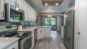 A modern kitchen with white cabinetry, stainless steel appliances, and a wooden ceiling. - Lakefront AND on the MTB trails! (Bella Vista)
