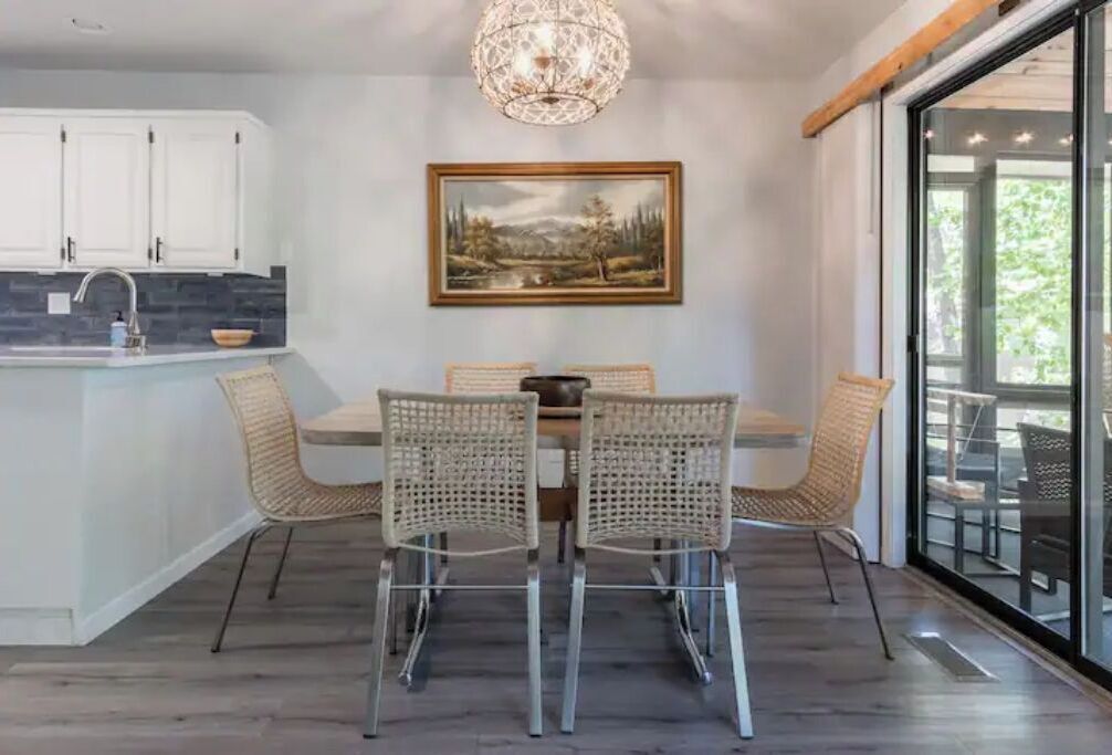 Un coin repas avec une table et des chaises, un tableau accroché au mur et une vue à travers une porte vitrée.