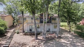 Een huis met twee verdiepingen en een balkon, omgeven door bomen en een grindpad.