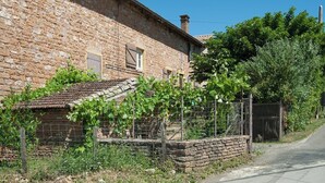 A rustic stone building with a small garden area, a brick wall, and a metal fence. - Le Bas de Leynes - LEYNES (LEYNES)
