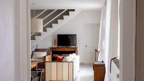A narrow hallway leading to a living area with a sofa, TV, and staircase. - Le Bas de Leynes - LEYNES (LEYNES)