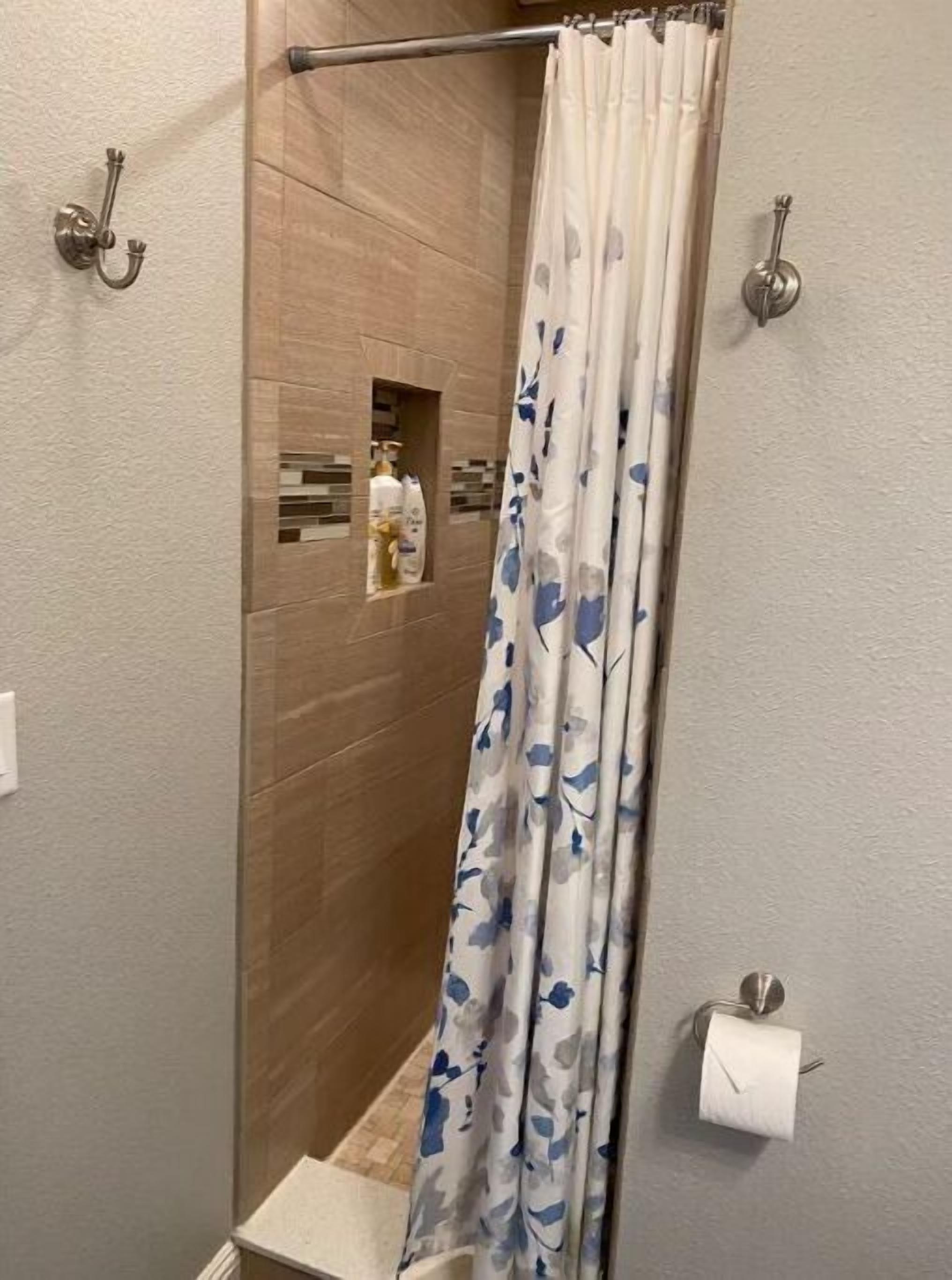 A shower with a wooden wall, a shower curtain with a floral pattern, and a towel rack with a roll of toilet paper.