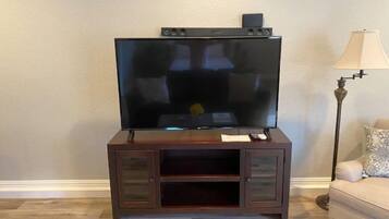 A flat-screen TV on a wooden TV stand with a remote and a small device on top.