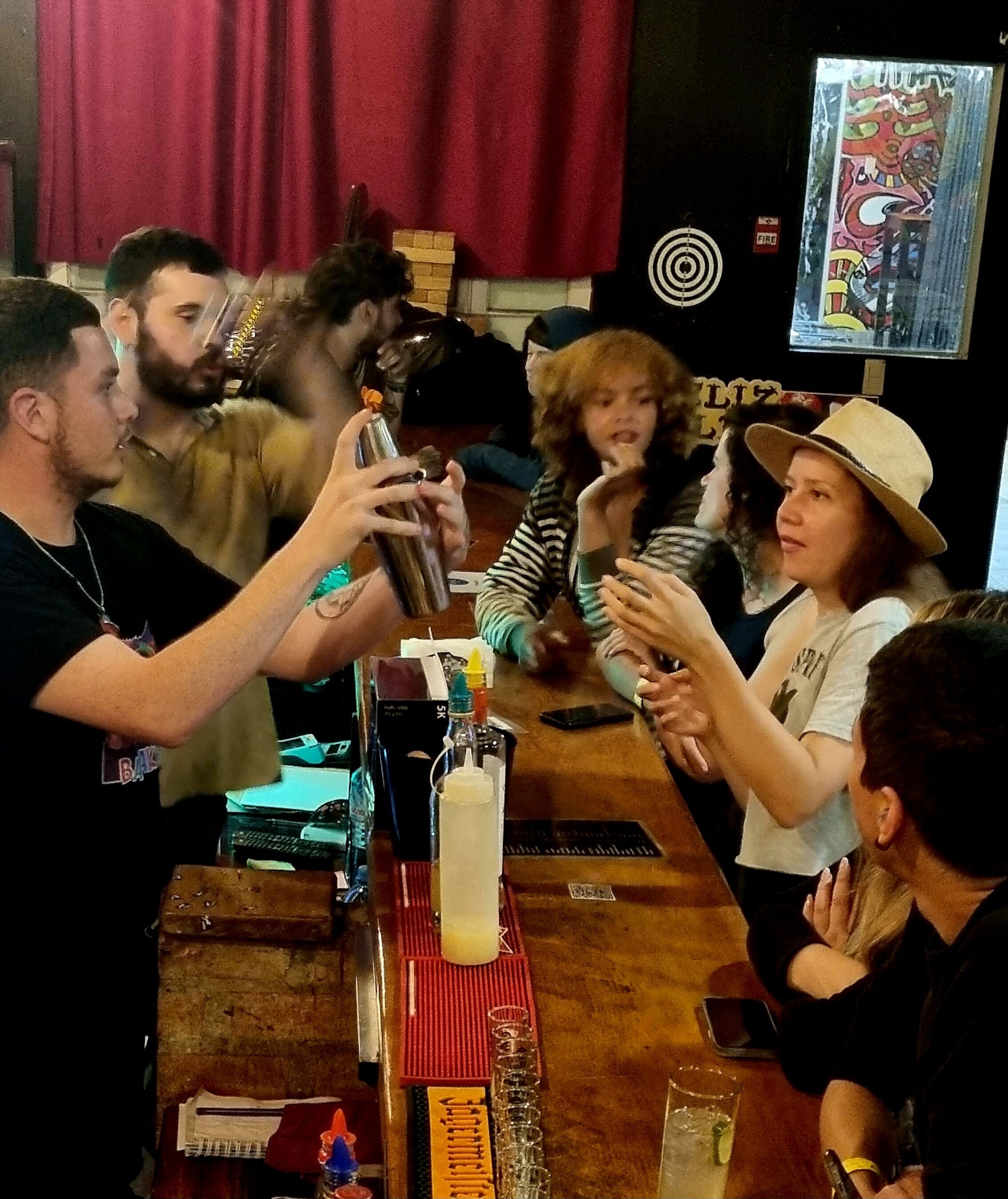 A bar setting with a bartender preparing drinks, a cash register, and various bar tools on the counter.