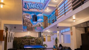 Um hall amplo com mesa de pingue-pongue, parede de escalada com plantas e um mural no teto.