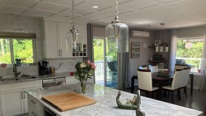 Una cocina con encimera de mármol, tabla de cortar de madera, un florero con flores y una lámpara colgante.
