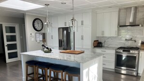 Una cocina moderna con armarios blancos, electrodomésticos de acero inoxidable y una isla central con taburetes de bar.