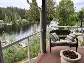 Un balcón con una silla de mimbre, un hogar a leña y vista a un lago con barcos.