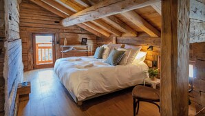 A cozy log cabin bedroom with a wooden bed, a nightstand, a chair, and a window with a view. - Chalet Sisar - ski-in ski-out break for 12, La Clusaz - OVO Network (La Clusaz)