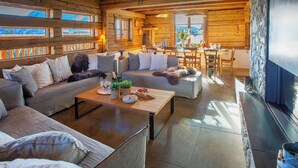 A cozy log cabin interior with a living area, dining space, and a stone fireplace. - Chalet Sisar - ski-in ski-out break for 12, La Clusaz - OVO Network (La Clusaz)
