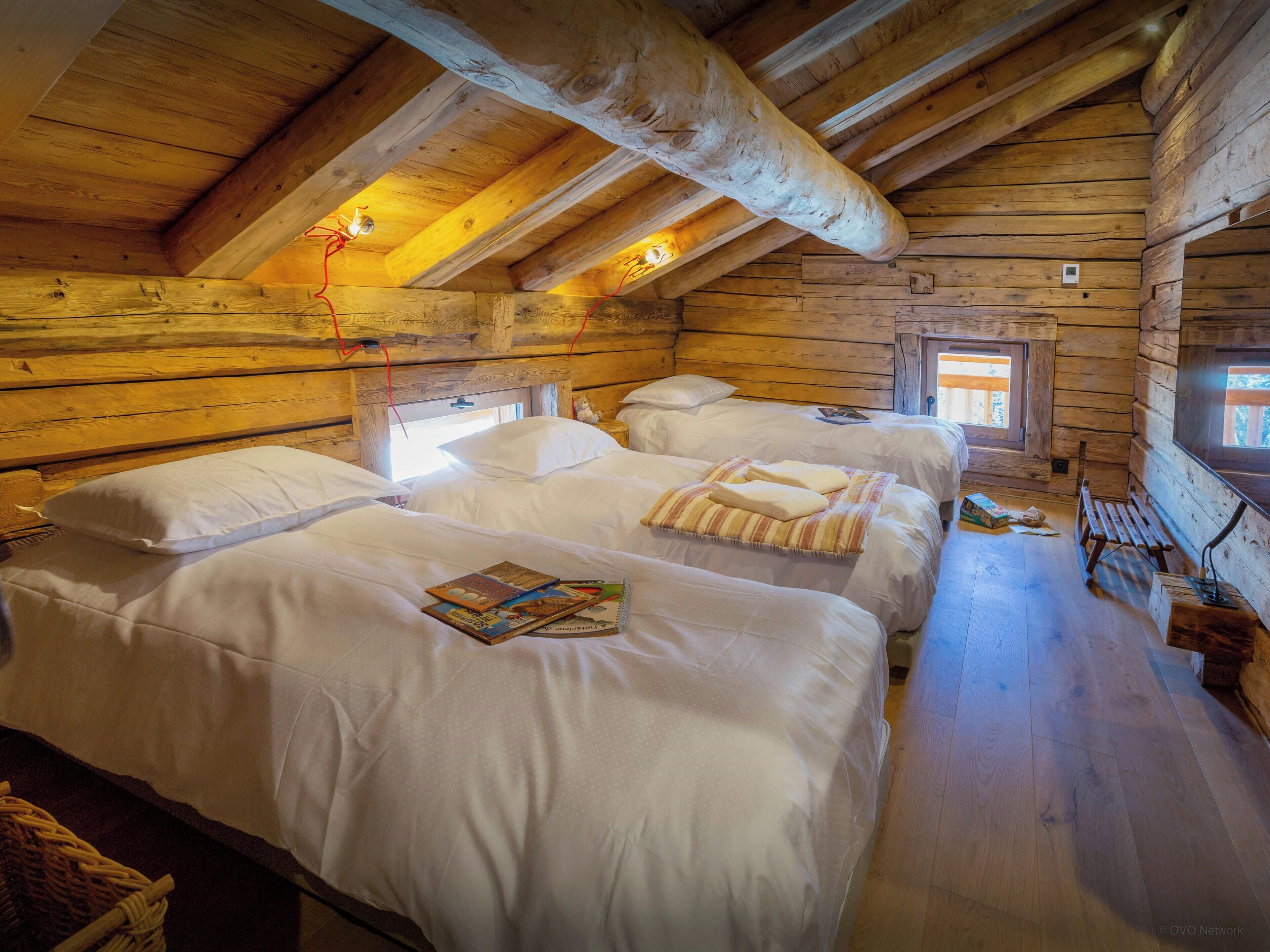 A log cabin bedroom with three beds, wooden beams, and a sloped ceiling.