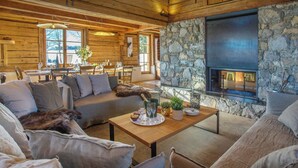 A cozy cabin interior with a stone fireplace, wooden furniture, and a dining area. - Chalet Sisar - ski-in ski-out break for 12, La Clusaz - OVO Network (La Clusaz)
