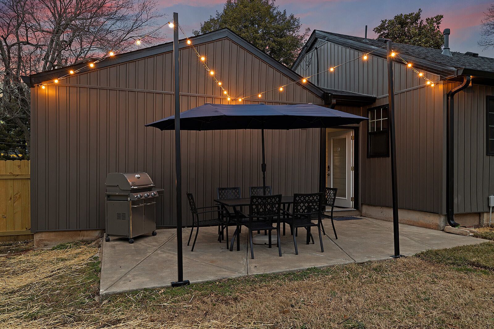 Patio sul retro con barbecue, tavolo da pranzo e sedie, riparato da una tettoia con luci decorative.