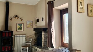 A room with a fireplace, a radiator, a chair, and a window with curtains. - Independent farmhouse within an organic farm, NIDO DEL GEPPIO (Lazio)