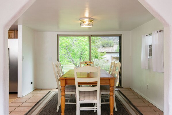 A dining area with a table and chairs, a ceiling light fixture, and a view through a glass door. - Relaxing Riverfront Taos Staycation, Pet Friendly! (Embudo)