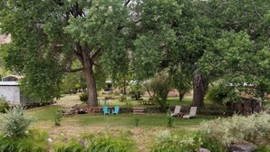 A serene outdoor area with a small stream, picnic tables, and chairs. - Relaxing Riverfront Taos Staycation, Pet Friendly! (Embudo)