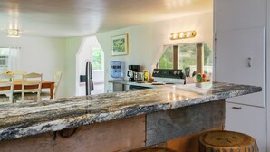 A kitchen with a granite countertop, wooden cabinets, and a water dispenser. - Relaxing Riverfront Taos Staycation, Pet Friendly! (Embudo)