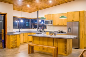 A modern kitchen with wooden cabinets, stainless steel appliances, and a large island with a bench. - Big Views, Pool, Extremely Private 4-Bdrm Home (Samara)
