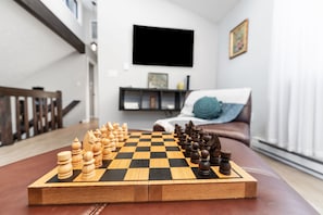 A chessboard set on a wooden table in a living room with a sofa and a TV in the background. - NEW Cozy Tobyhanna Getaway w/ Firepit & Hot Tub Near Waterparks! (Tobyhanna)