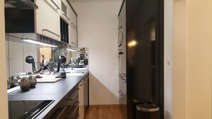 A narrow kitchen with a black refrigerator, stainless steel appliances, and a wooden floor.