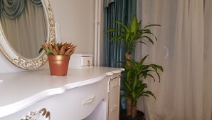 A white vanity with a gold-framed mirror, a copper pot with succulent plants, and a tall green plant in a black pot.