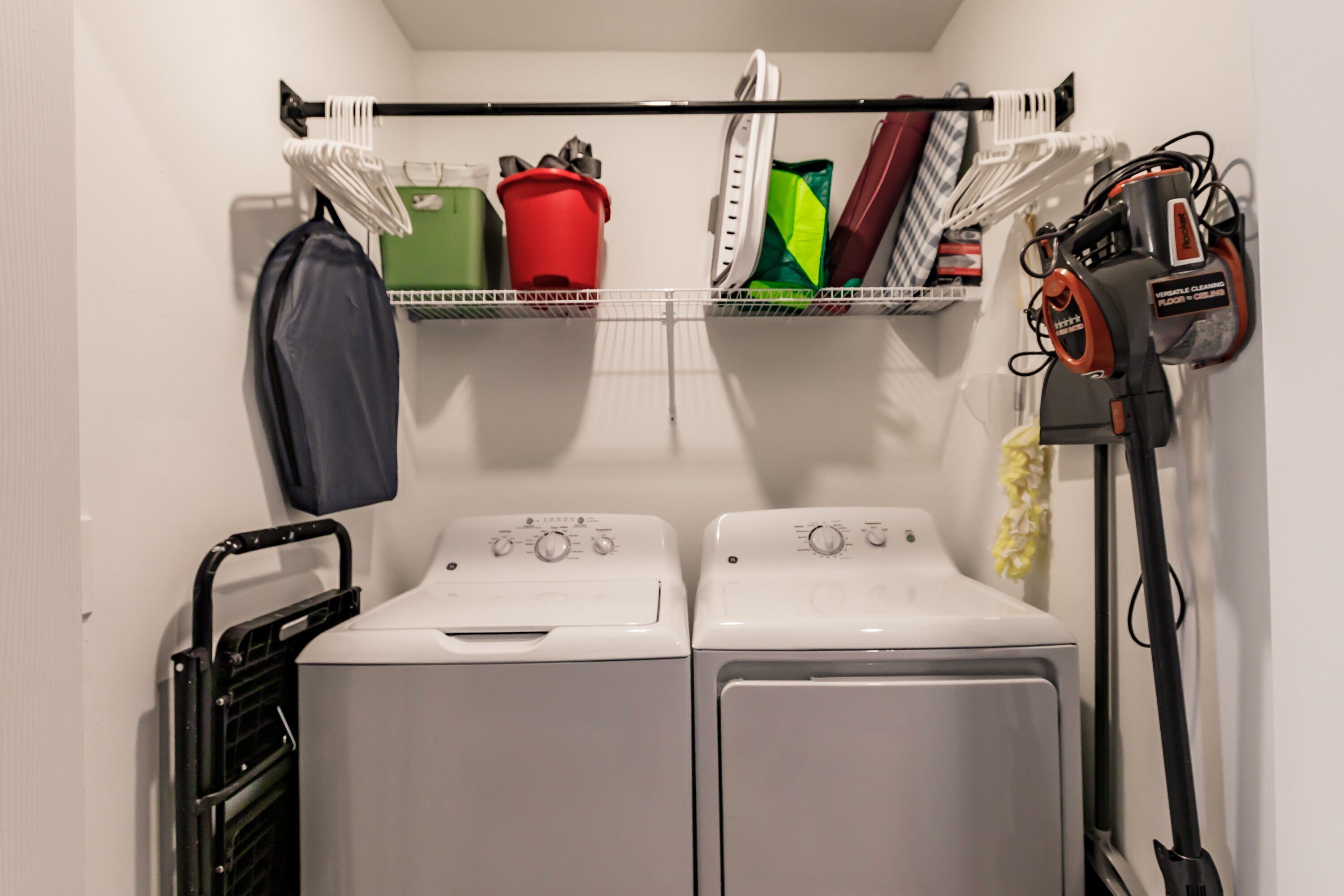Un espace buanderie équipé de deux machines à laver, d’un étendoir et d’un aspirateur.